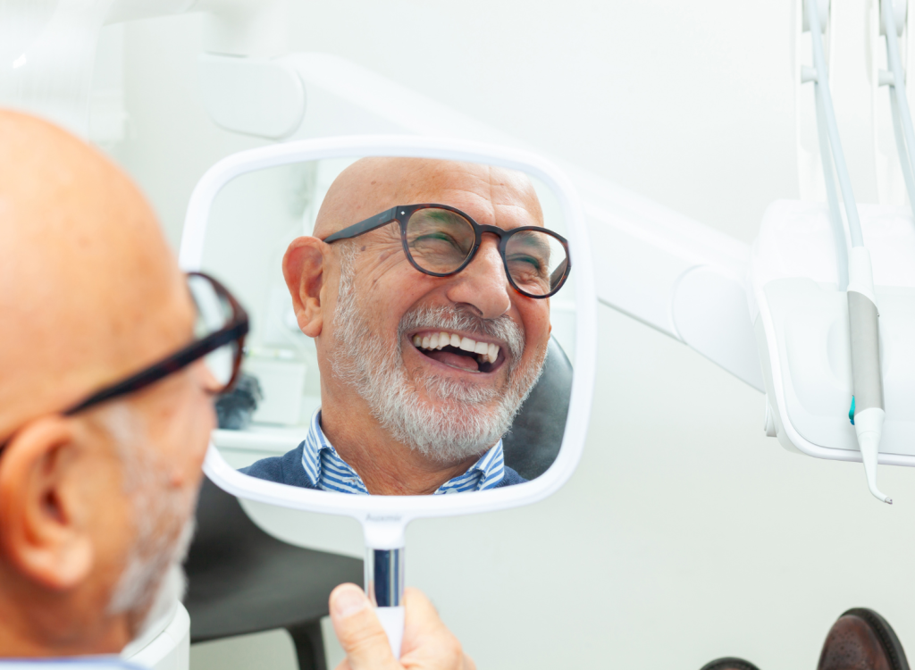 Man holding mirror, smiling, after having completed their full mouth implant procedure